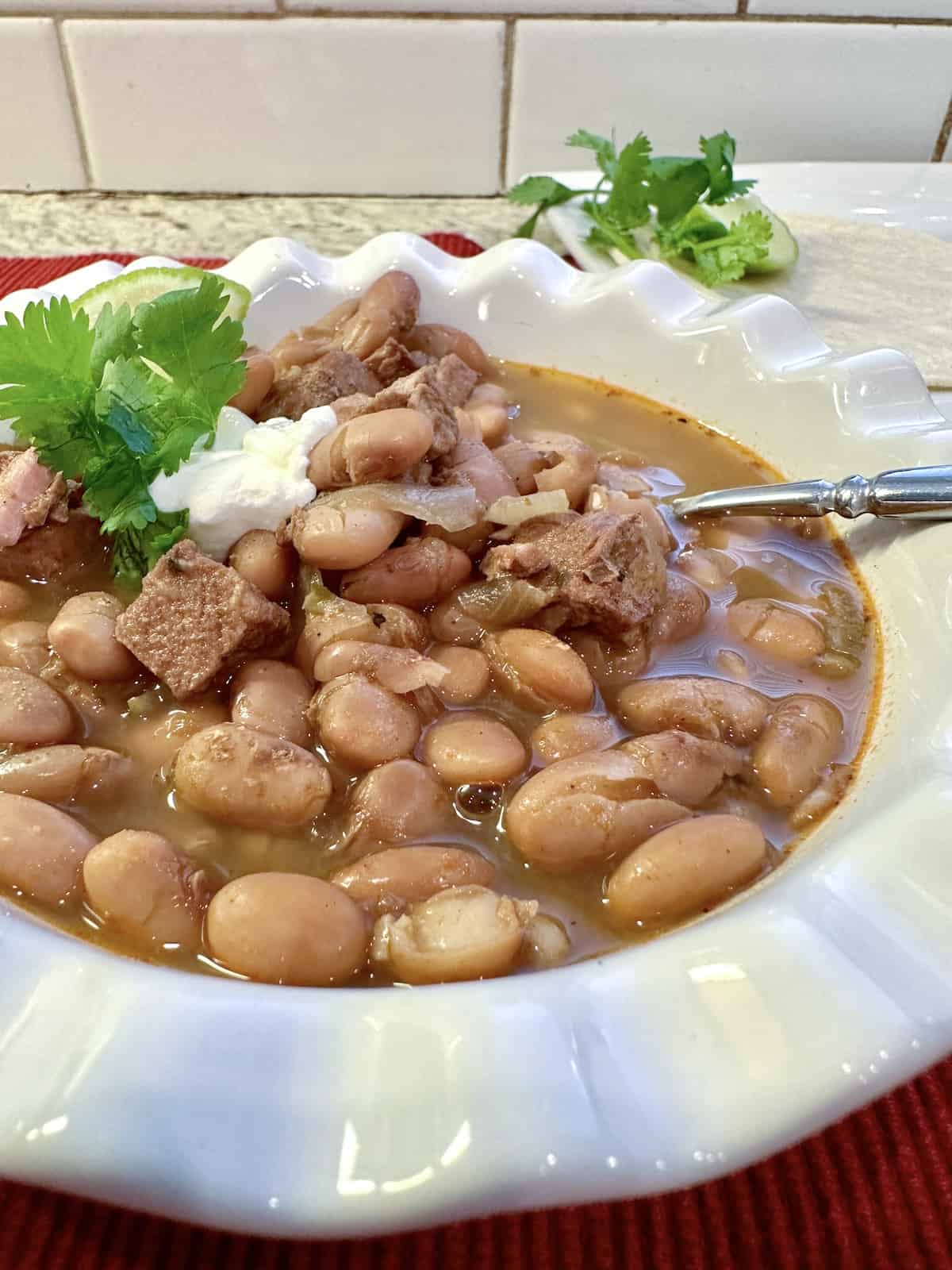 A serving of pinto bean chili in a bowl with a spoon and garnishes on the side.