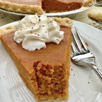A slice of pumpkin pie with the pie in the background.