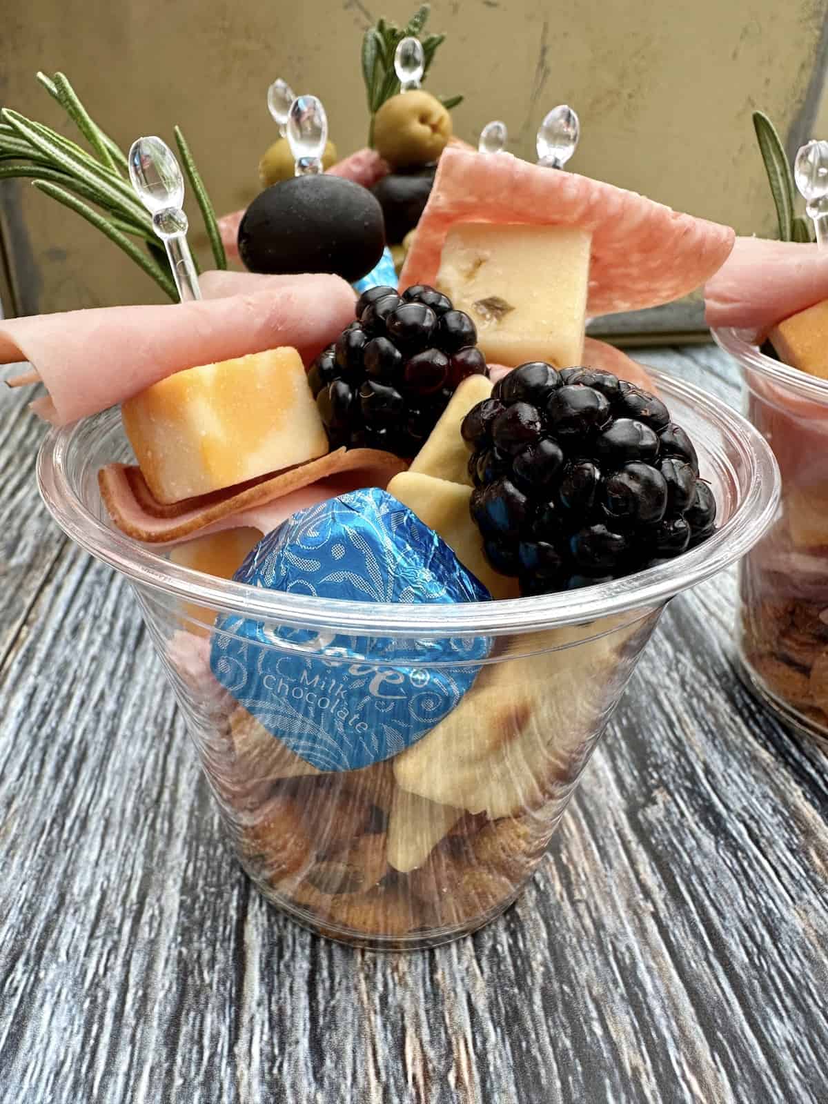 Cheese, crackers, meat, olives stacked in a cup.