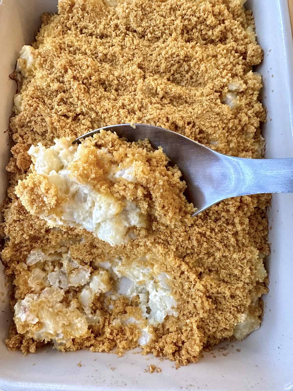 A serving spoon scooping up a serving of potato casserole from a baking dish.