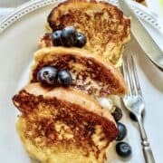 Three slices of buttermilk french toast on a plaste with berries on top.