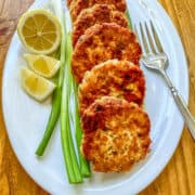 Cooked salmon patties on a plate with scallions, lemons and a fork.