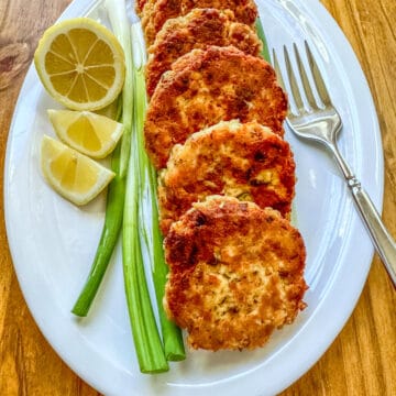 Cooked salmon patties on a plate with scallions, lemons and a fork.