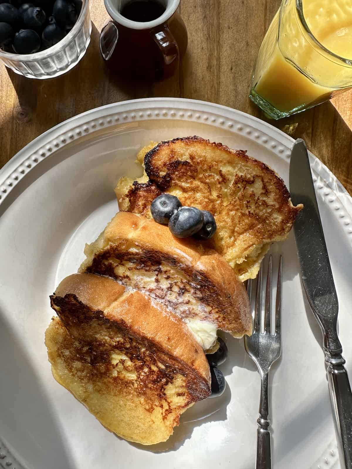 Several slices of french toast on a plate with berries, orange juice and syrup.