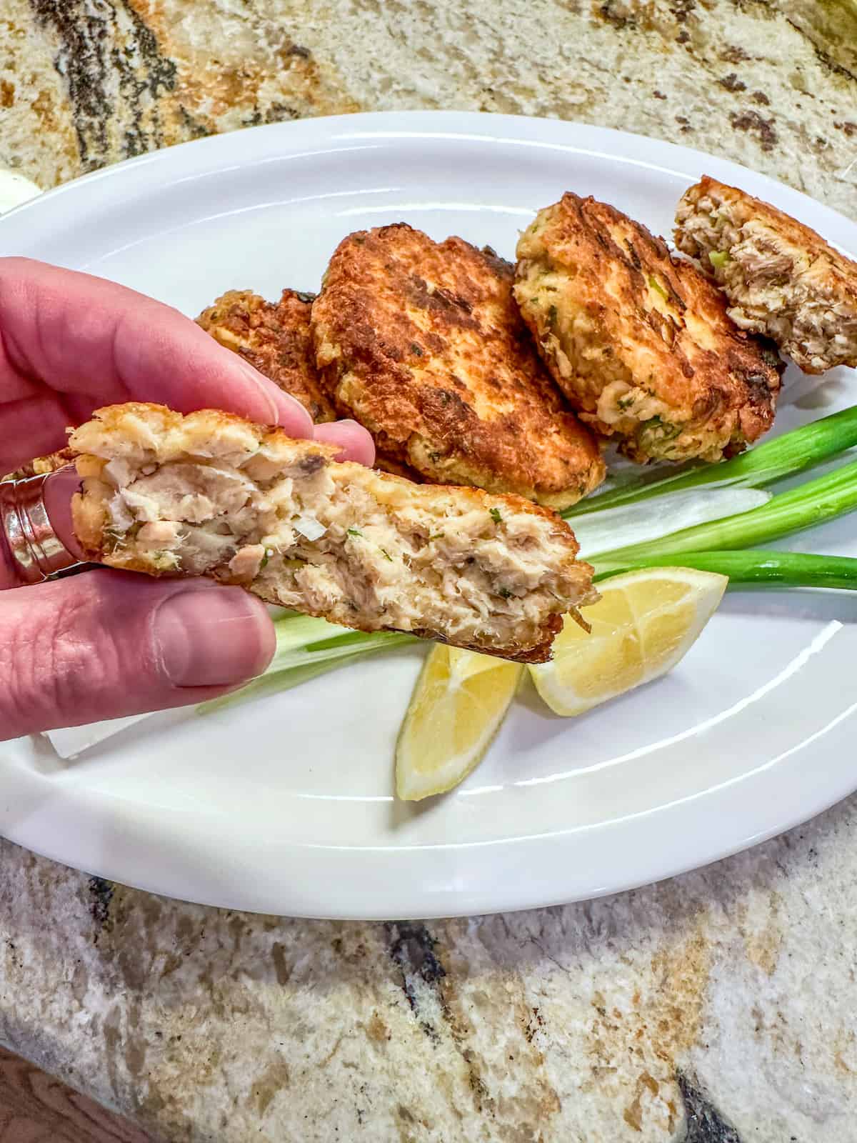 A salmon patty cut in half and held in a hand over a plate.