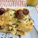 A serving of cheese, egg and sausage casserole on a plate with a glass of orange juice.