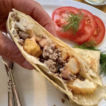 A hand holding a half of a French Taco over a plate.