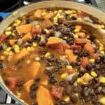A pot on the stove full of black bean soup with a spoon.