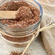 A small jar full of taco seasoning with a spoon on top and a napkin.