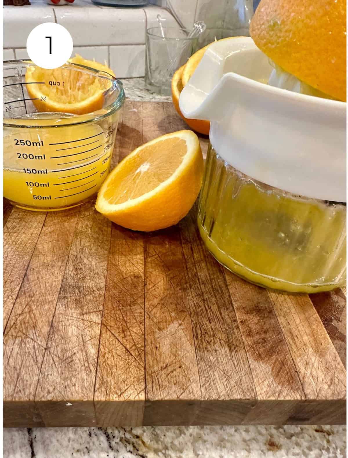 Oranges sliced in half with orange juice in a container on a cutting board.