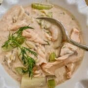 A bowl of creamy seafood chowder with fresh dill on top and a spoon.