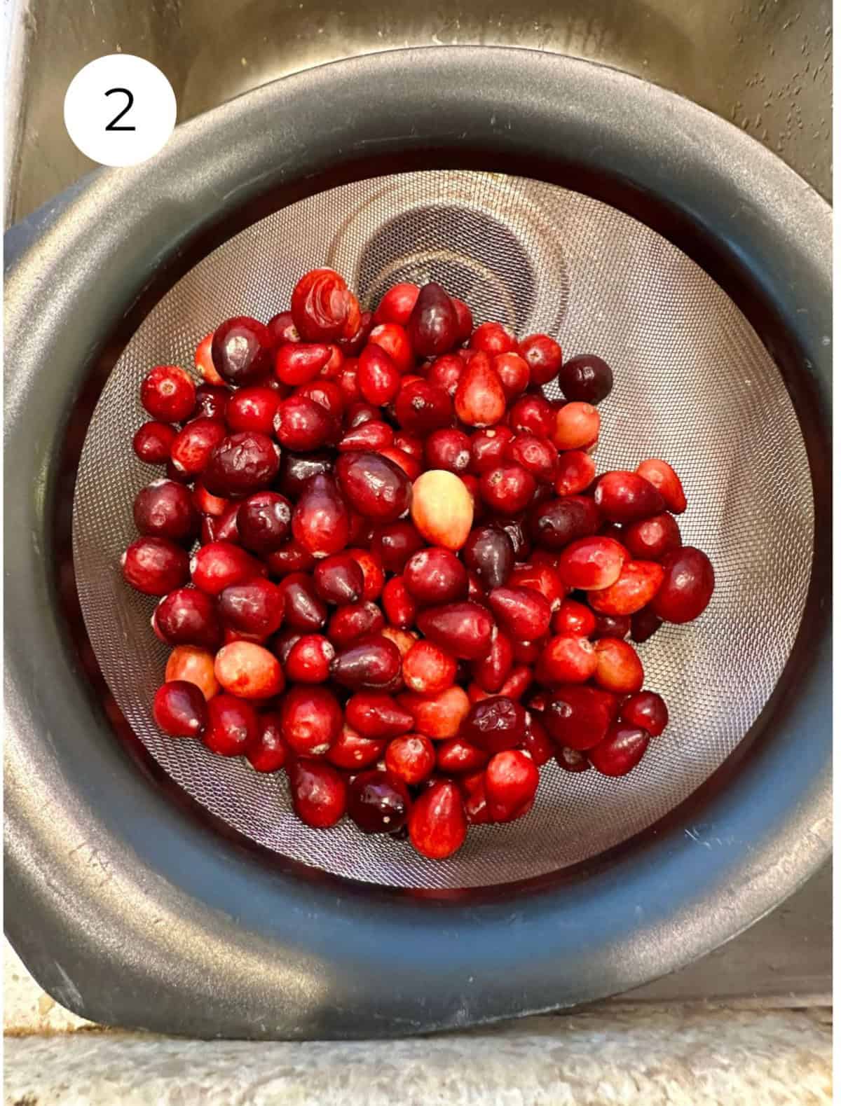 Fresh cranberries in a strainer over a sink.