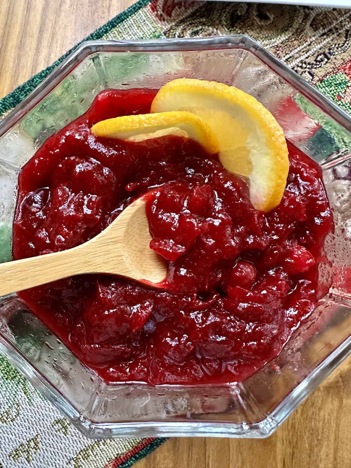 Two slices of orange in a bowl of cranberry orange sauce with a spoon.