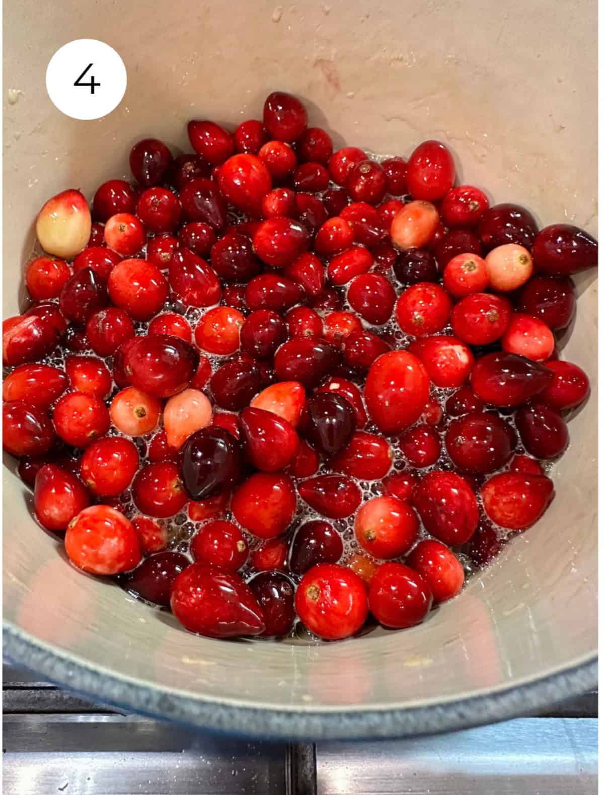 Fresh cranberries with liquid ingredients in a pan on the stove.