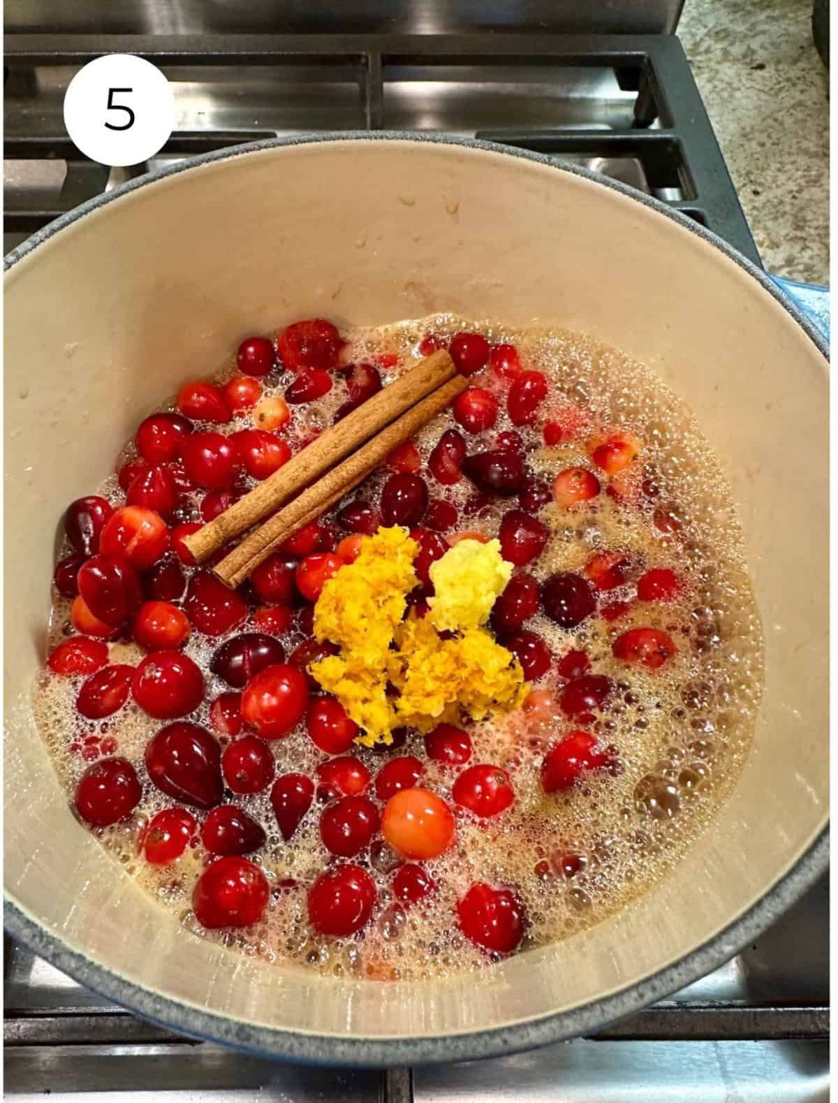 Cranberries with orange zest and cinnamon sticks in a pan on the stove.