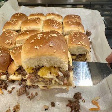 A spatula serving a cheeseburger slider from a baking pan on the stovetop.