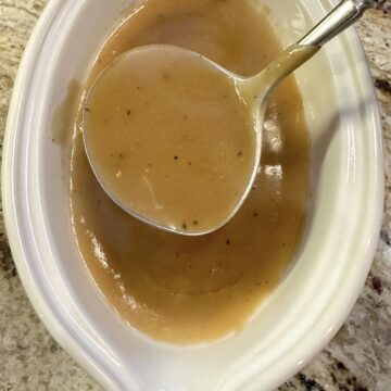 A gravy spoon in a serving bowl of gravy.