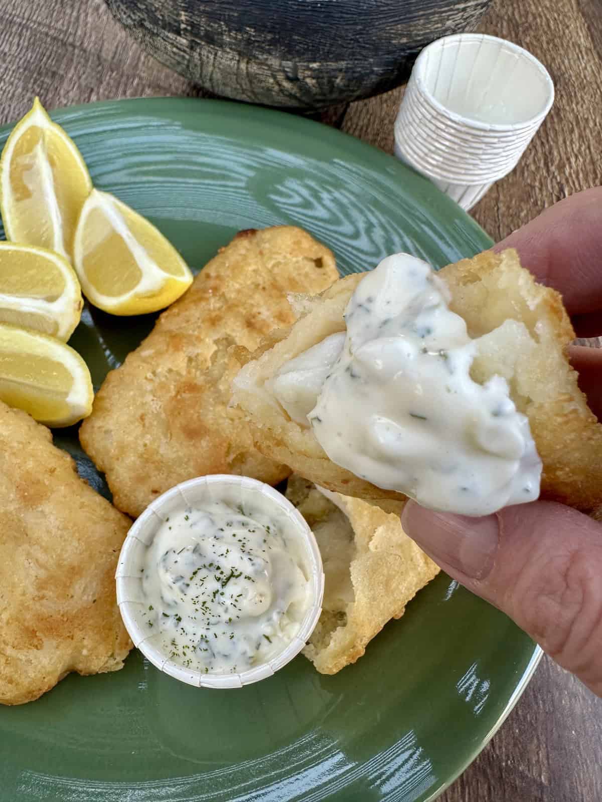 Fried fish and a small cup of tartar sauce on a plate.