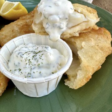Tartar sauce in a small cup on a plate with fried fish.