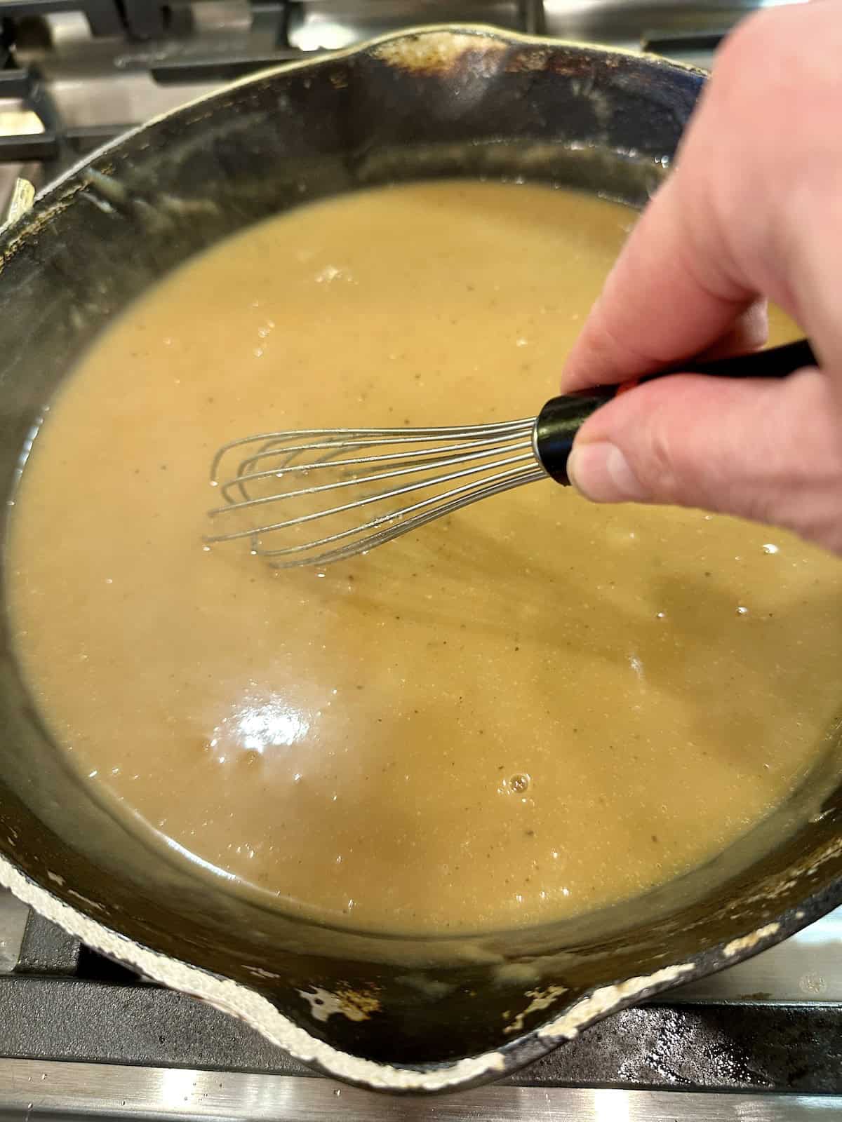 A skillet full of gravy with a whisk.