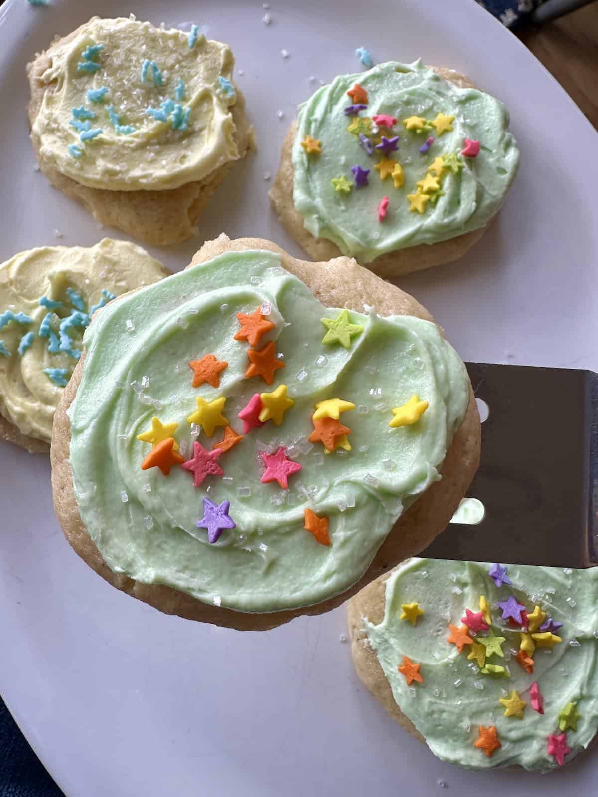 A frosted sour cream cookie on a spatula over a plate of cookies.