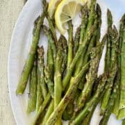 Pan roasted asparagus on a plate with lemon slices.