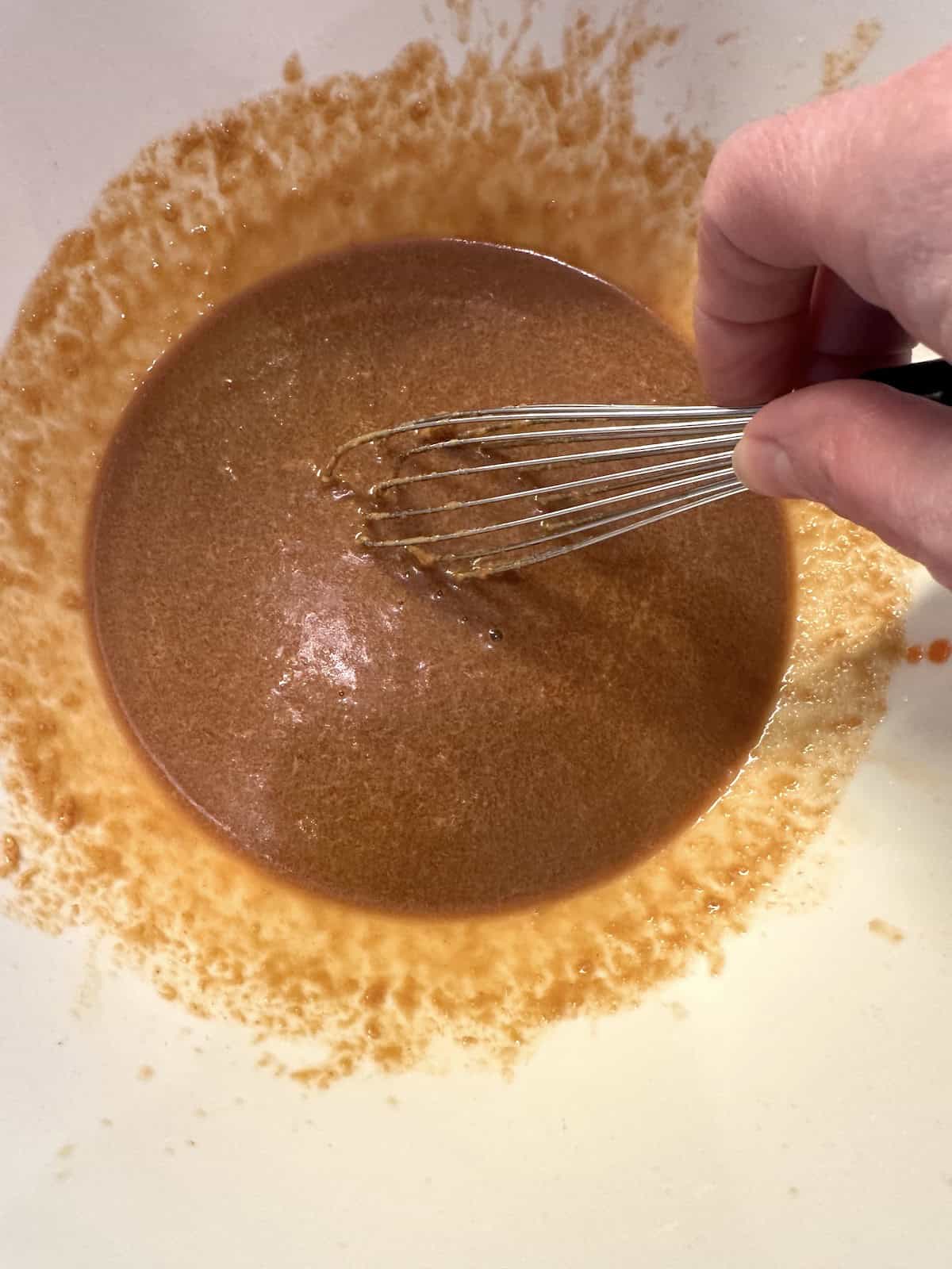 Blended spicy peanut sauce in a bowl with a whisk.