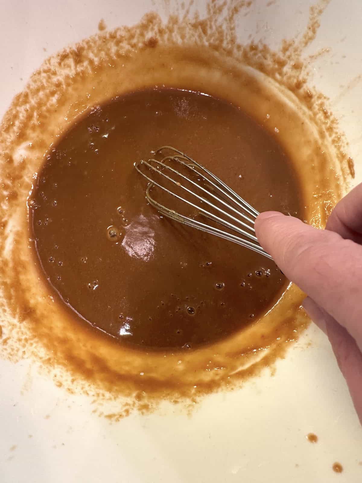 Peanut spicy noodle sauce in a bowl with a whisk.