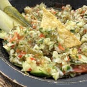 A bowl of pickle salsa with a tortilla chip on top.