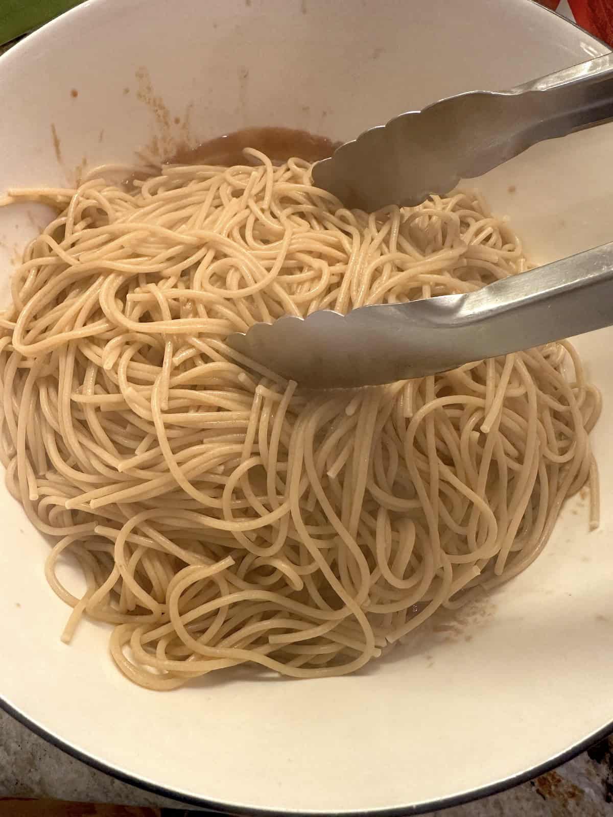 Cooked spaghetti in a bowl with tongs.