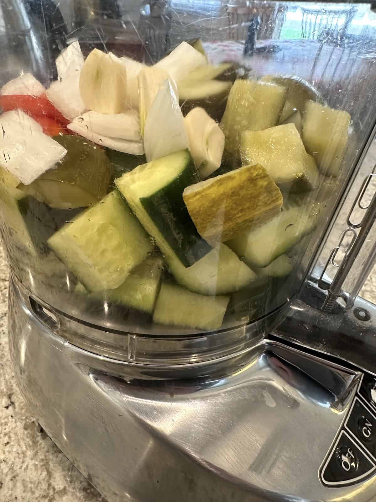 Pickles, cucumbers and onions in the bowl of a food processor.