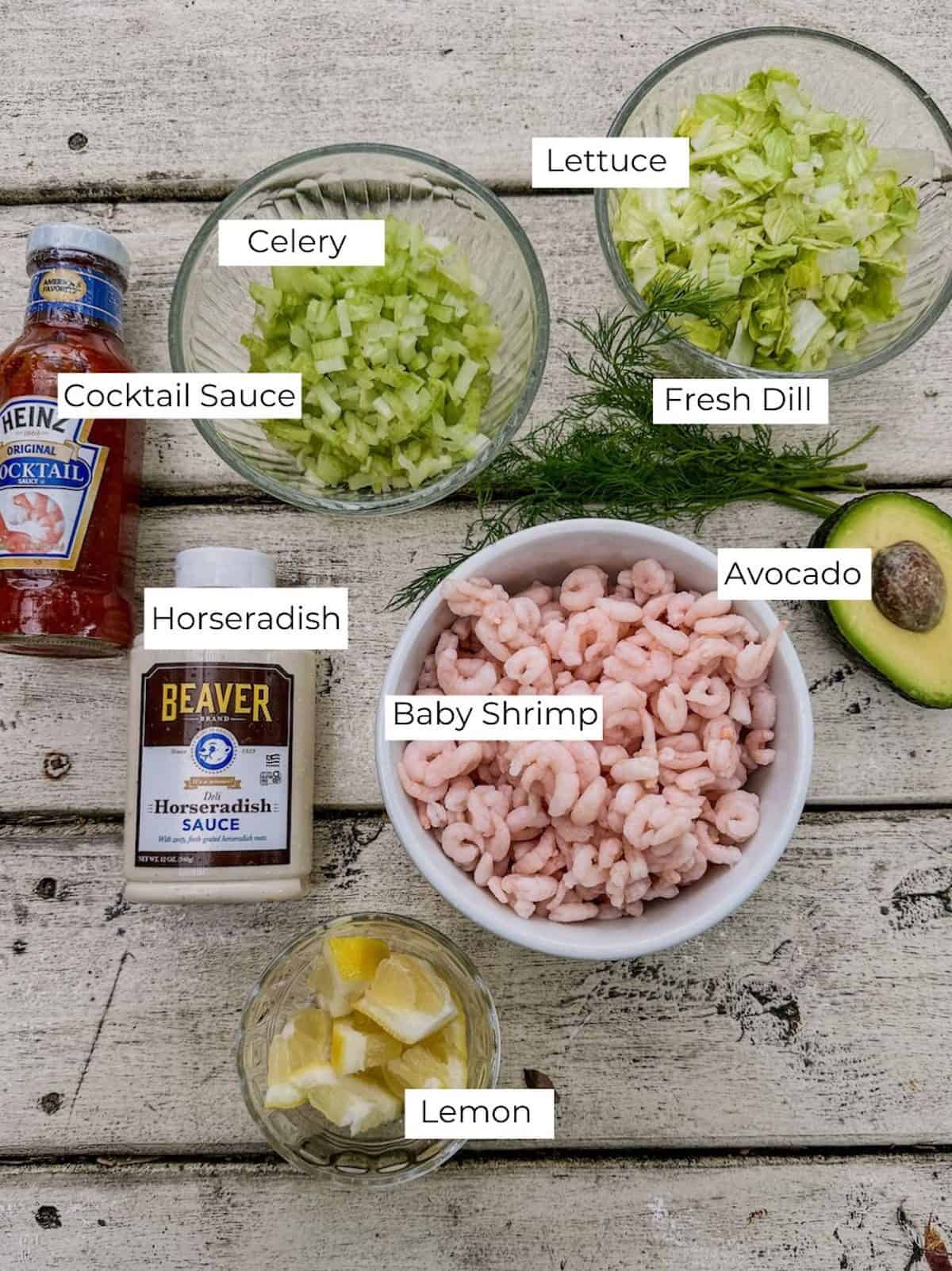 Labeled ingredients for shrimp cocktail cups on a wooden table.