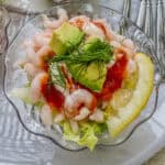 A small bowl of shrimp cocktail with lettuce, lemon, celery and avocado.