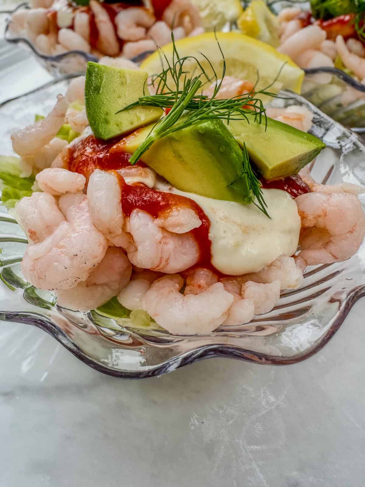Shrimp cocktail cups with fresh dill and sliced avocado on top.