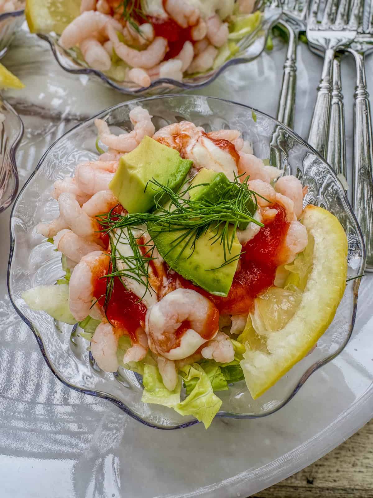 Shrimp cocktail in a small serving bowl with a slice of lemon, avocado and fresh dill.