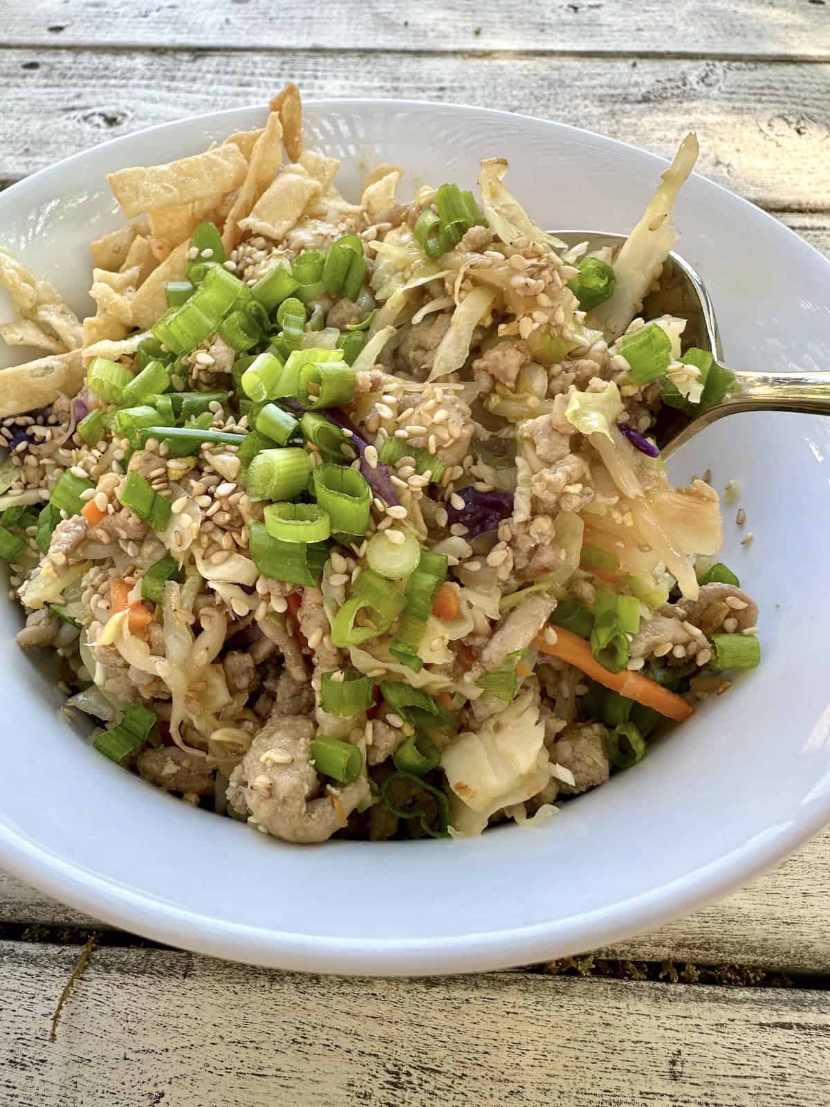A spoon scooping up a serving of spring roll in a bowl.