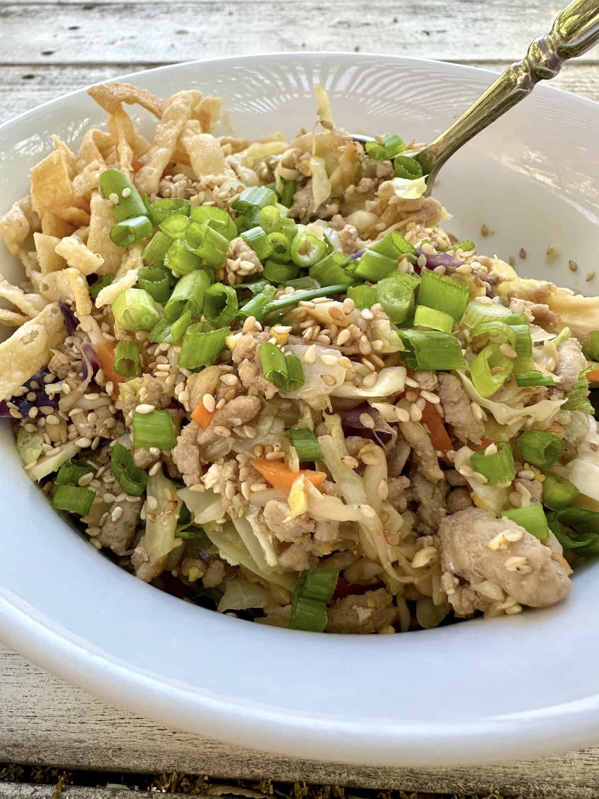 A serving of spring roll in a bowl with a spoons dishing up a scoop.