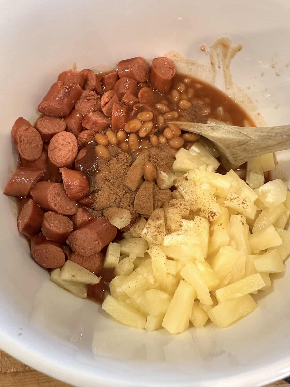 Ingredients for franks and beans in a large bowl.