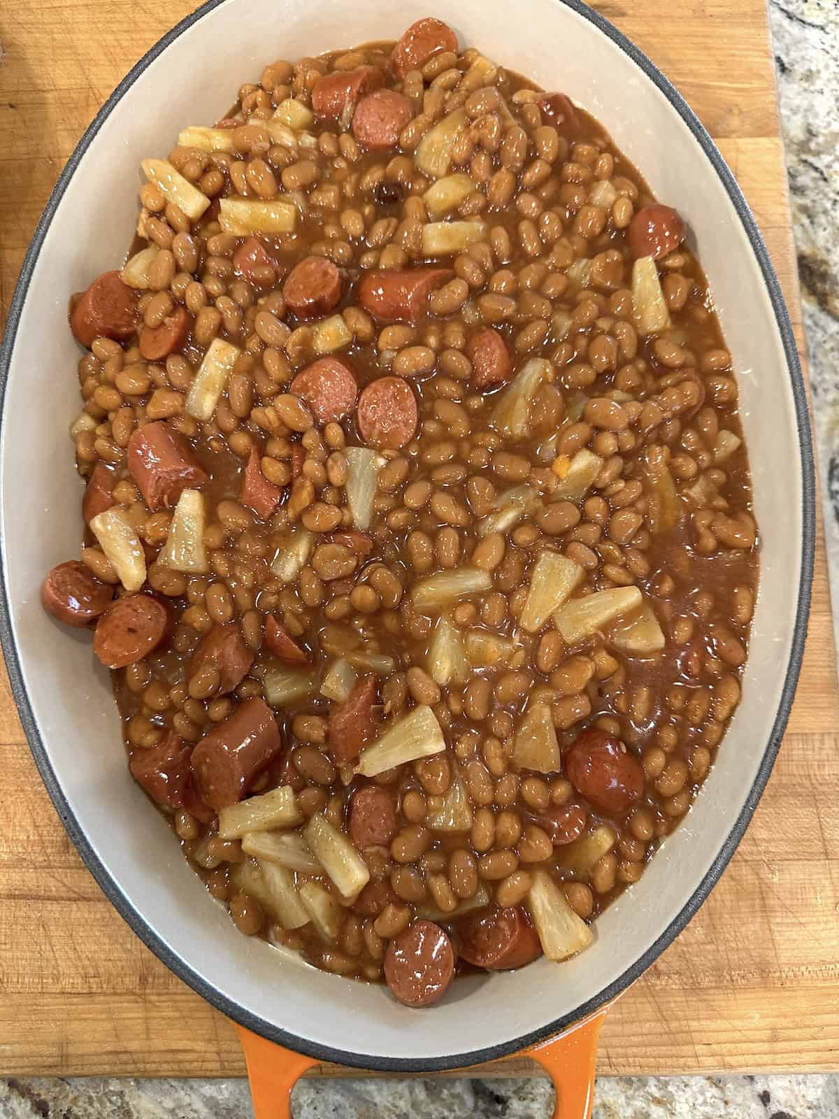 A pan filled with beans and hot dogs on a cutting board.