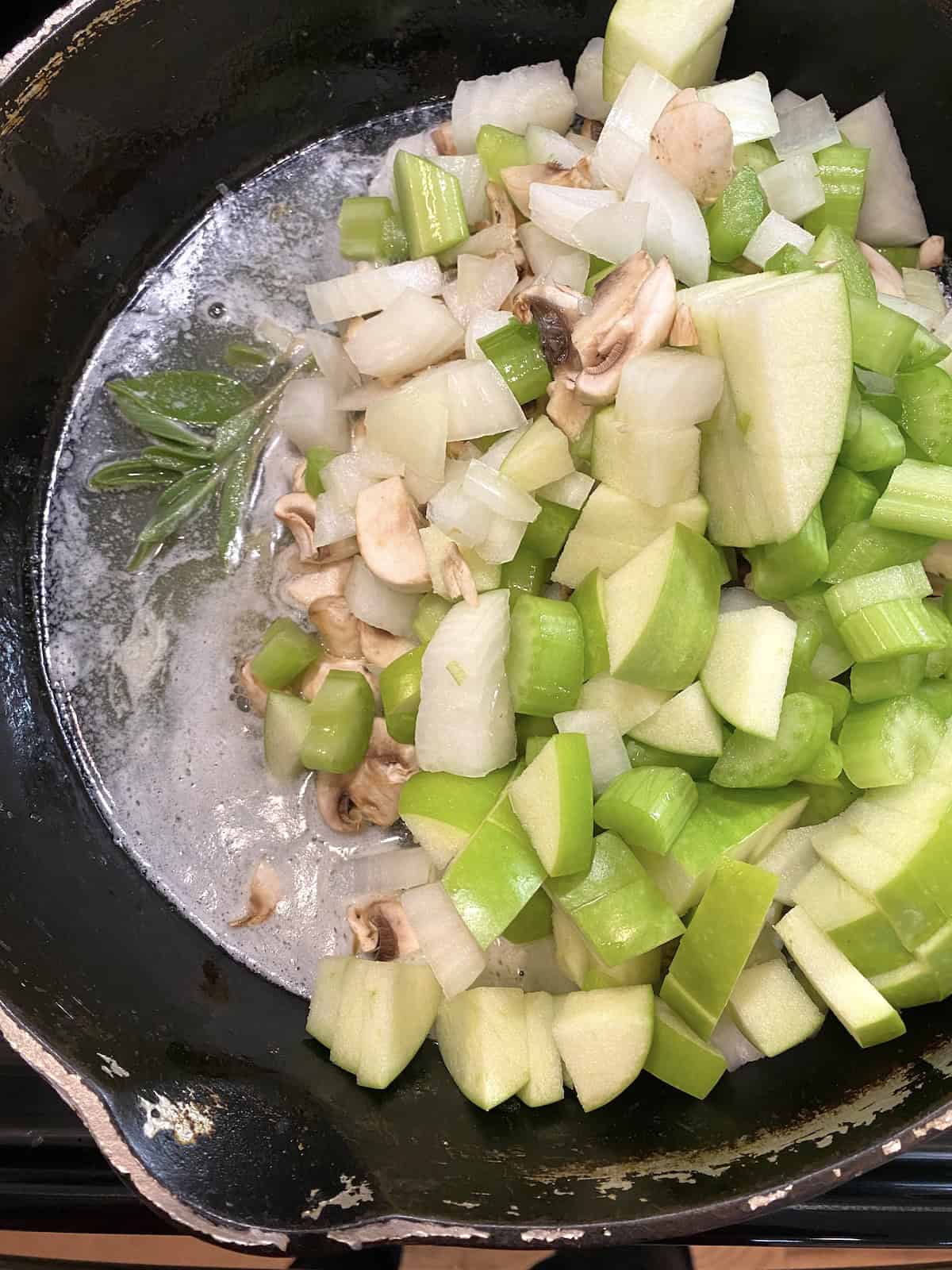 A skillet filled with chopped onions, mushrooms and celery.