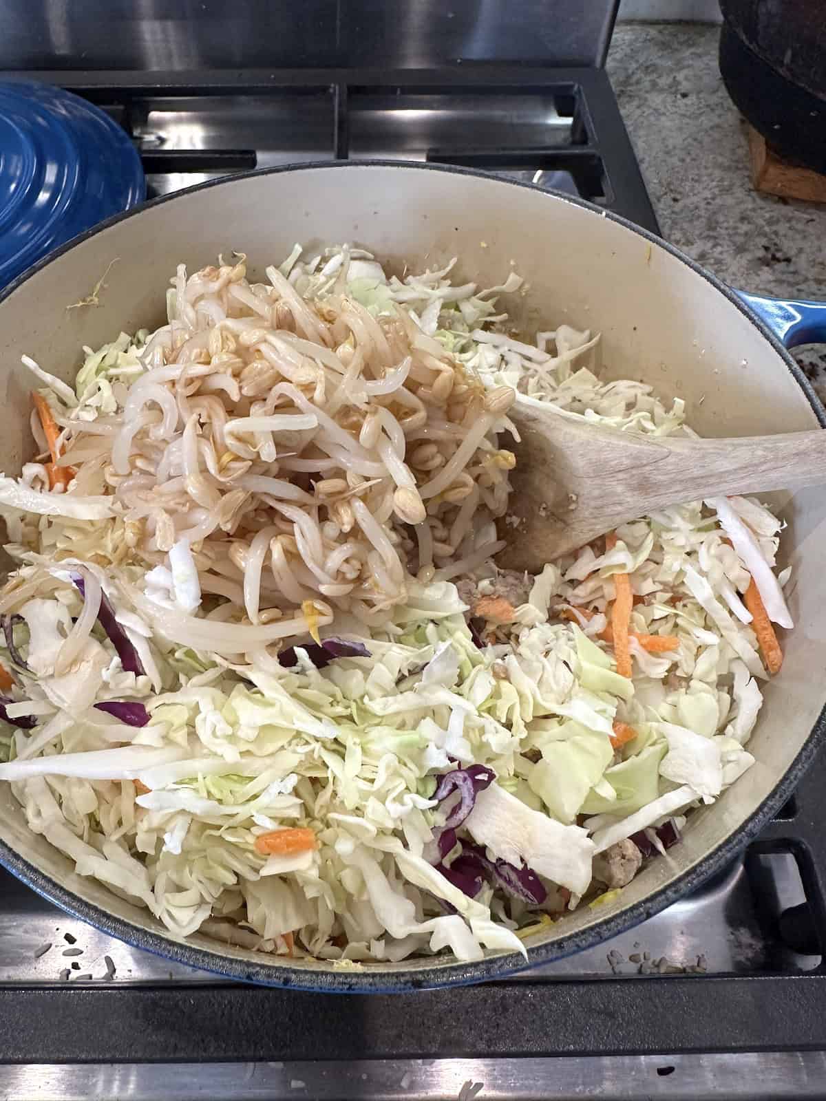 Bean sprouts and cabbage added to a pan of ground turkey on the stove.