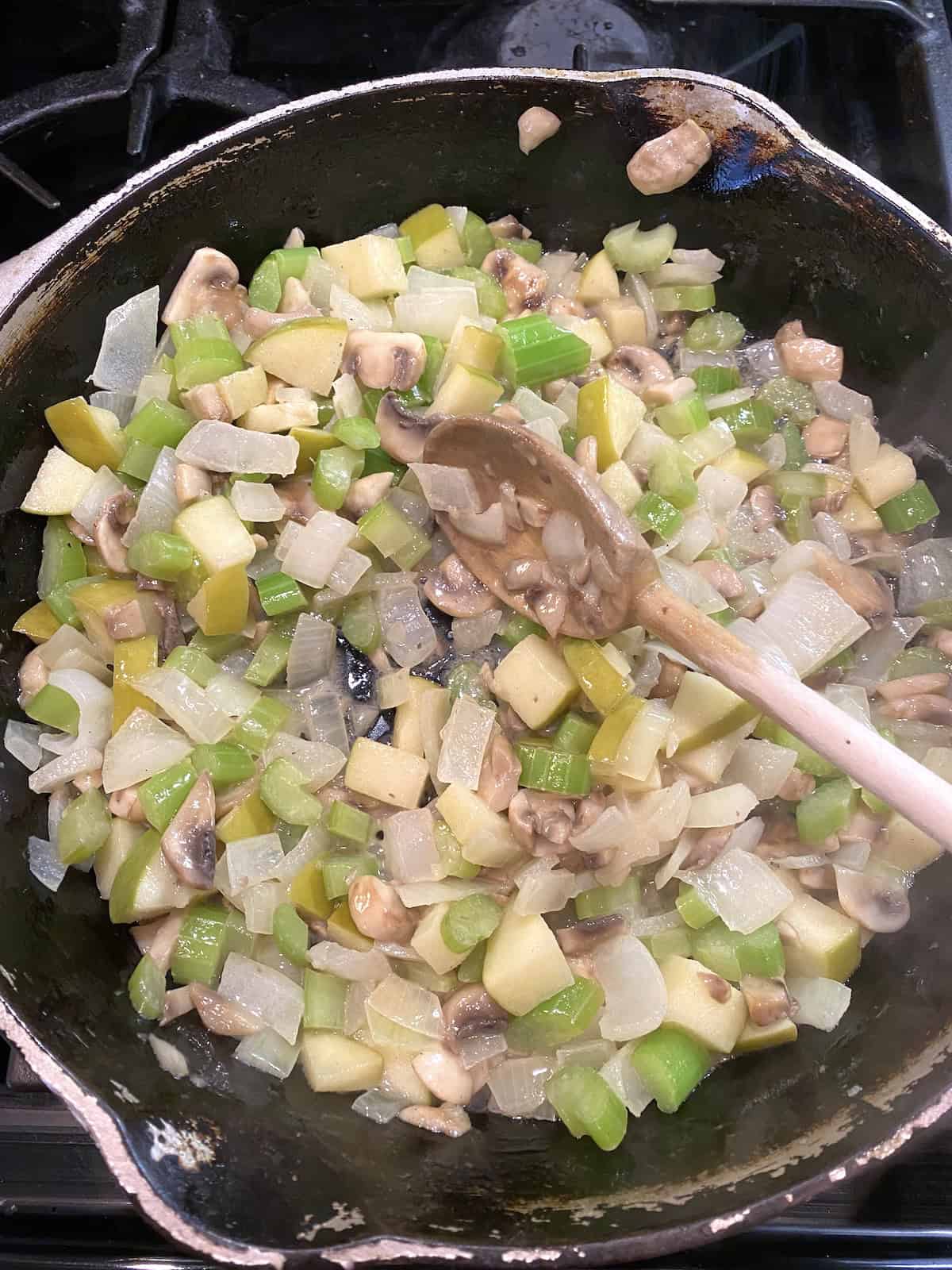 A skillet filled with vegetables, apples and mushrooms.