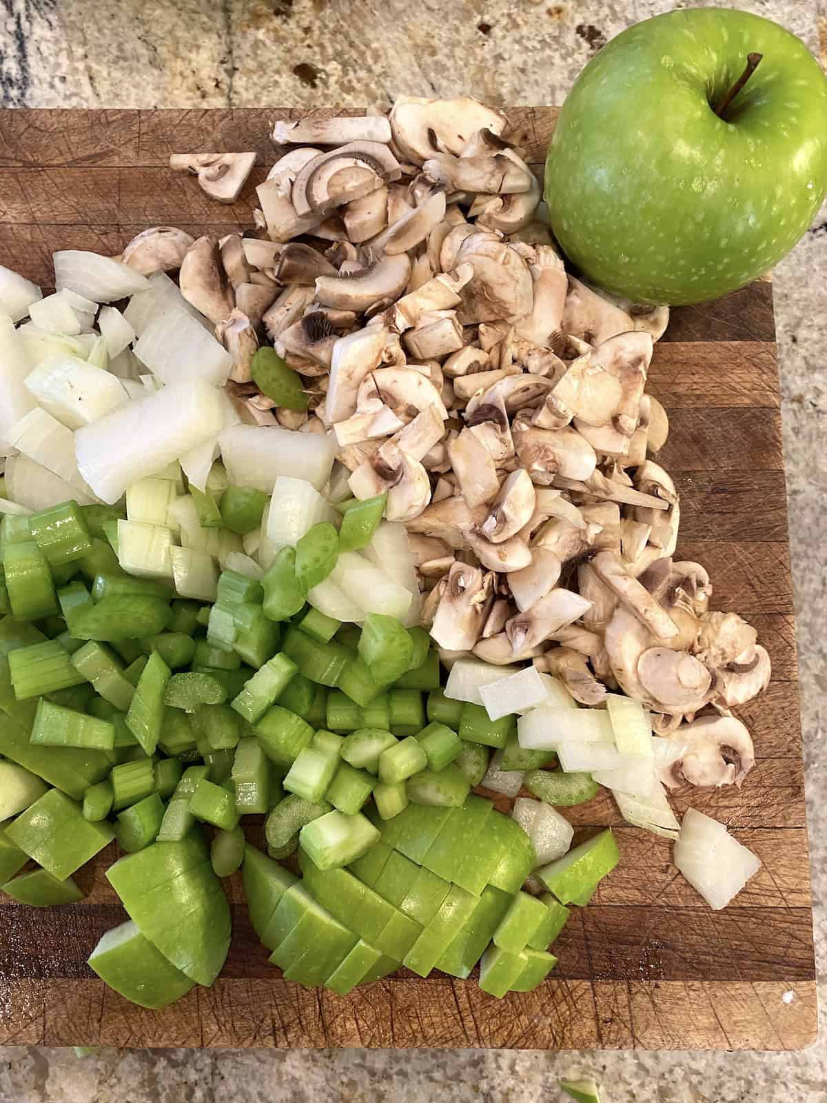 Chopped onions, mushrooms, and apples on a cutting board.