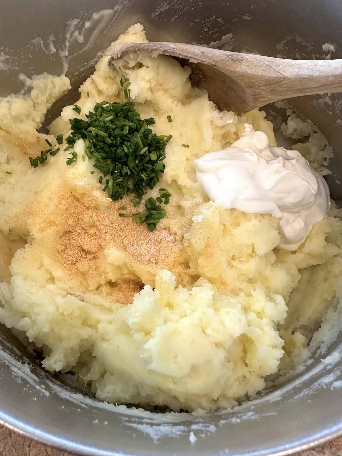 Mashed potatoes with sour cream, diced chives and garlic powder in a pot.