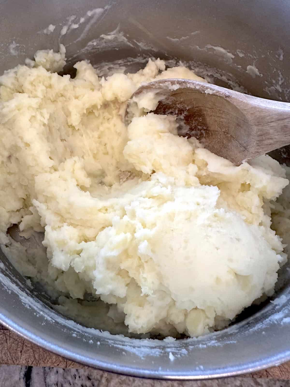 Potatoes in a pan, mashed with a wooden spoon.
