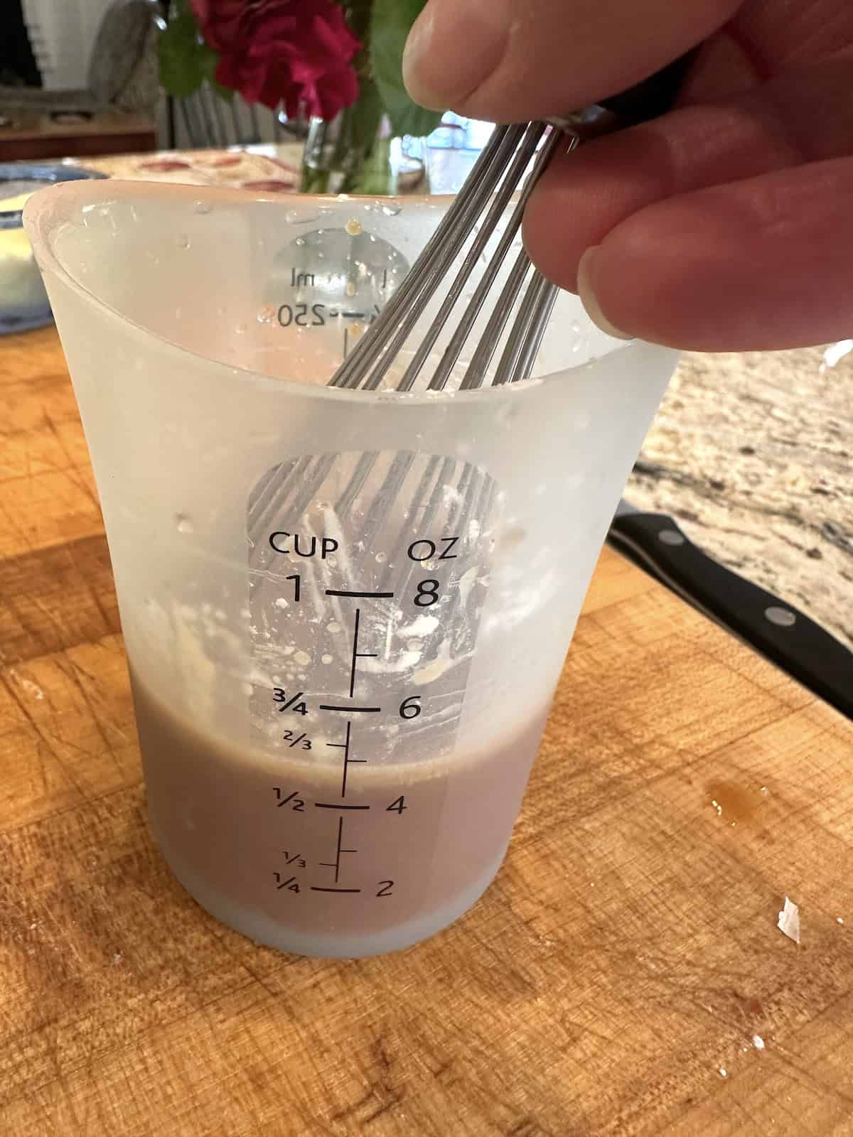 Sauce ingredients for spring roll in a bowl in a measuring up with a whisk on a cutting board.
