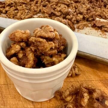 Spiced walnuts in a small jar next to to a baking pan.