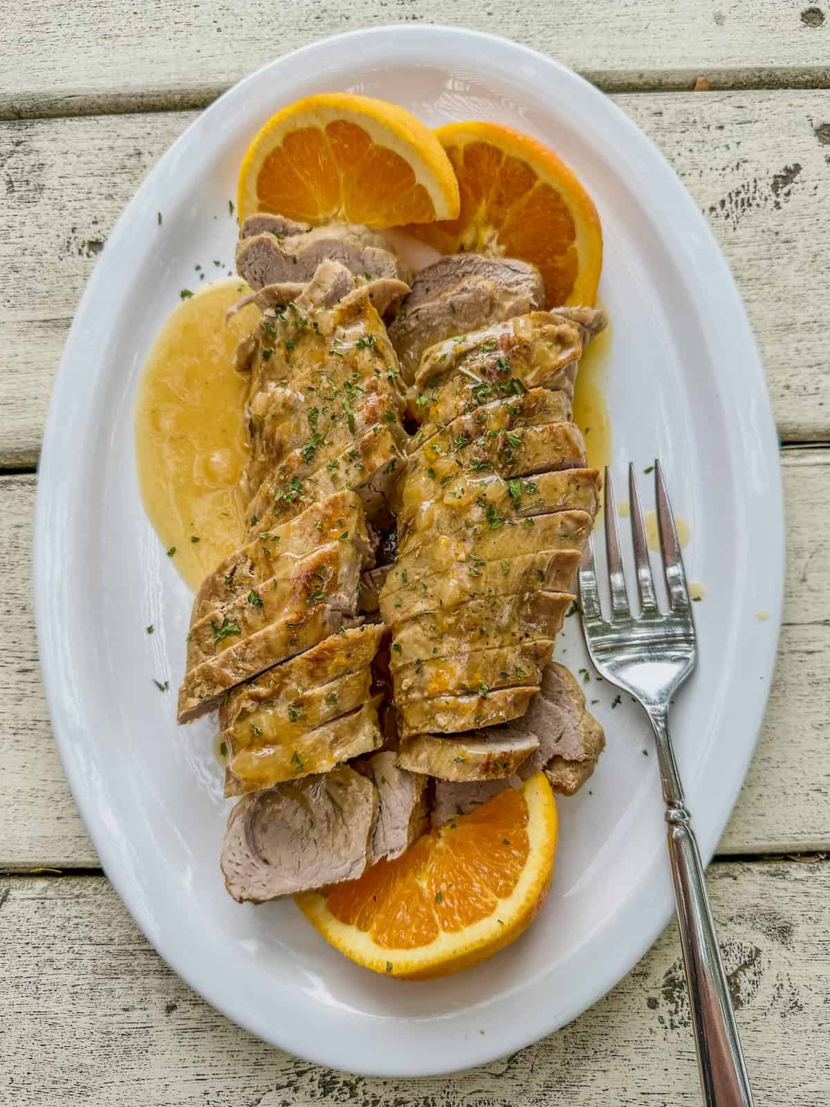 Orange glazed pork tenderloin slices on a serving plate with sliced oranges.