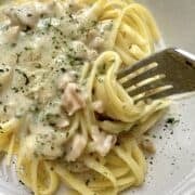 A serving dish of white clam sauce with a fork and pasta.