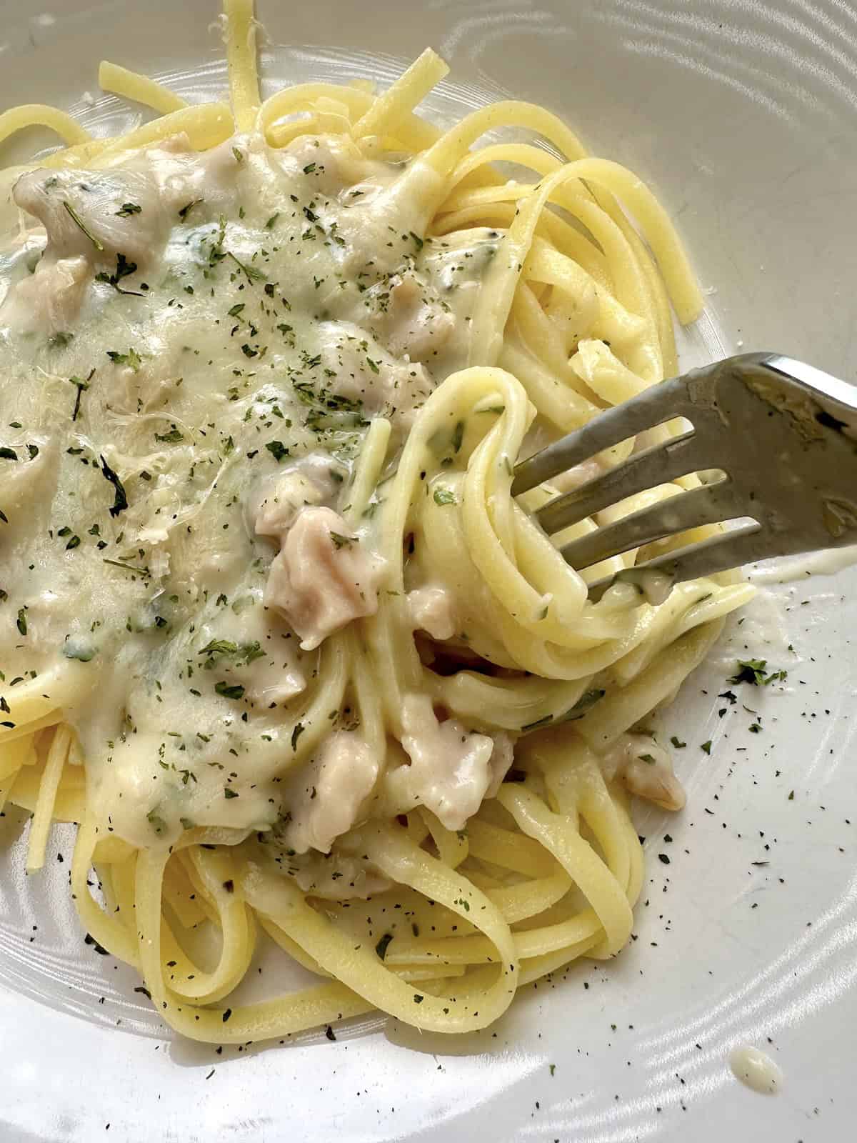 A serving dish of white clam sauce with a fork and pasta.
